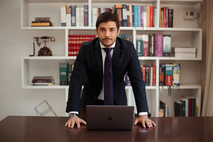 De terno escuro, de pé à mesa de trabalho, diante de uma estante de livros jurídicos.